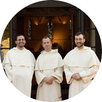 3 Dominican friars stand outside of a church