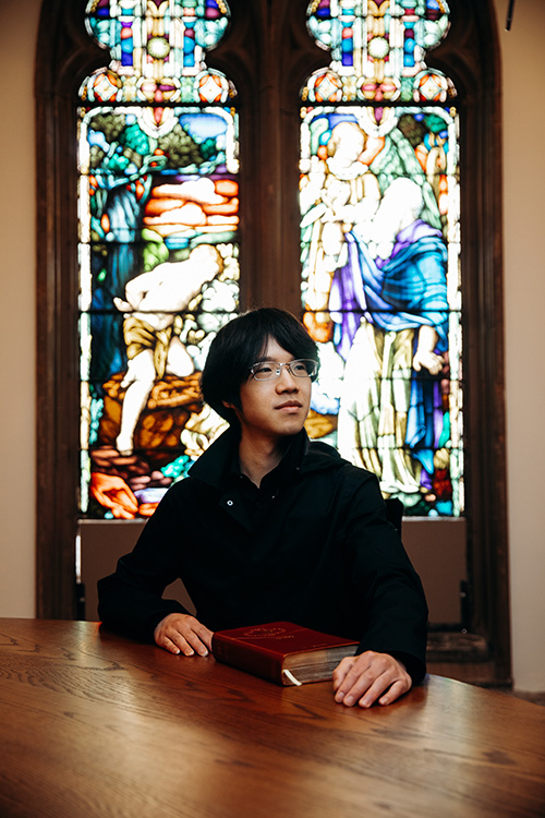 A graduate student sits in front of stained glass