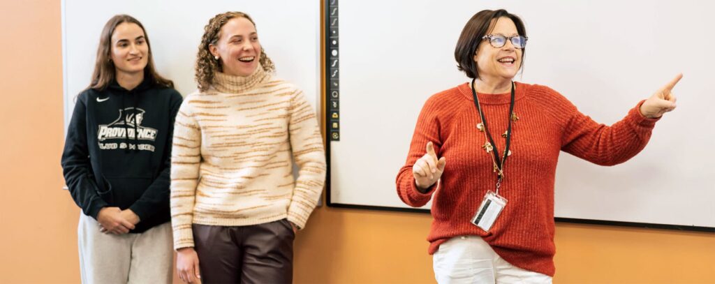 A professor works with two students in front of a smart board