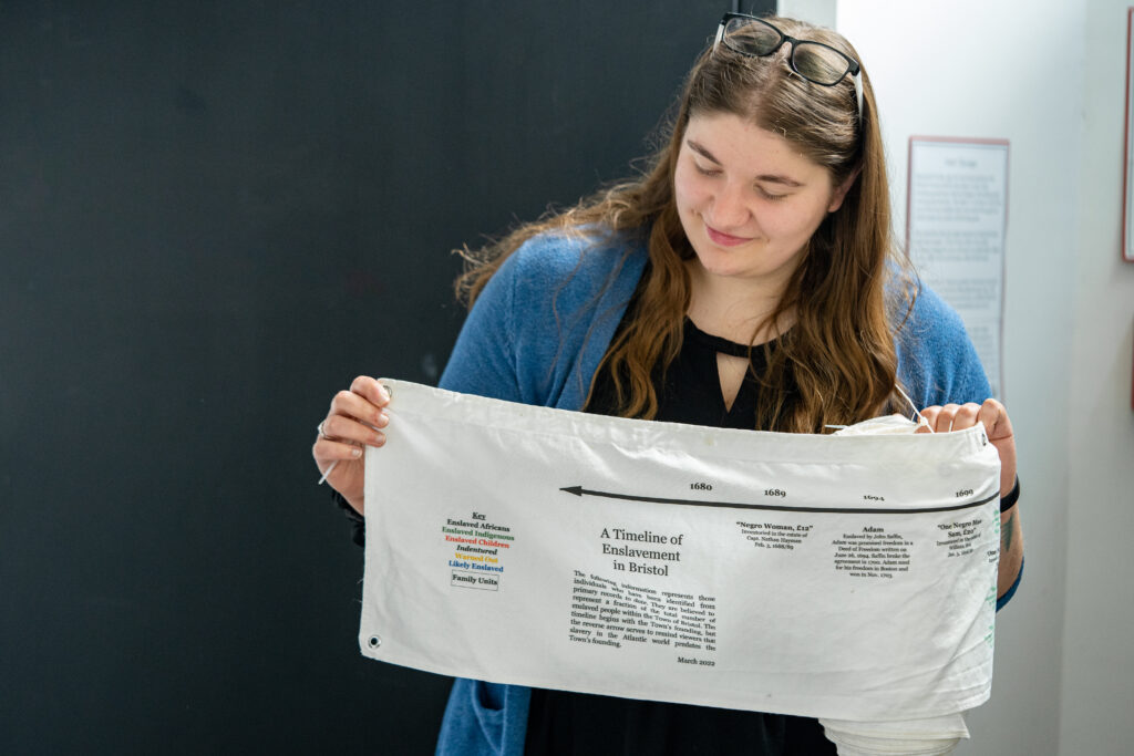 Courtney Garrity holding a flag representing a timeline of enslavement in Bristol.
